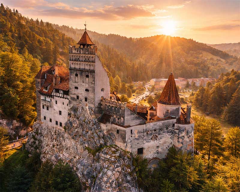 Hrad Bran pri východe slnka, hrad na skale obklopený lesmi, letecký pohľad zhora