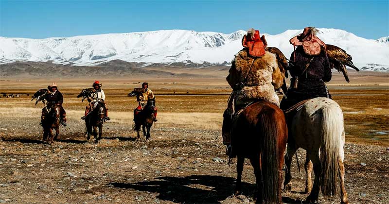 Tradičný život v Mongolsku, jazdci na koňoch s orlami v otvorenej stepnej krajine