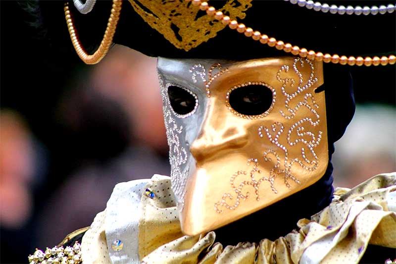 Detail zlatej benátskej karnevalovej masky s ornamentmi a historickým klobúkom