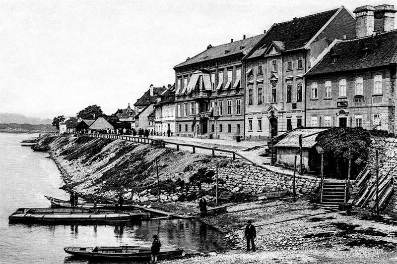 Staré mestské nábrežie s historickými budovami a člnmi na rieke, dobová fotografia