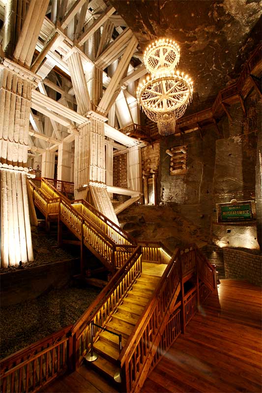 Drevené schodisko a masívna banská konštrukcia v Soľnej bani Wieliczka osvetlená lustrami